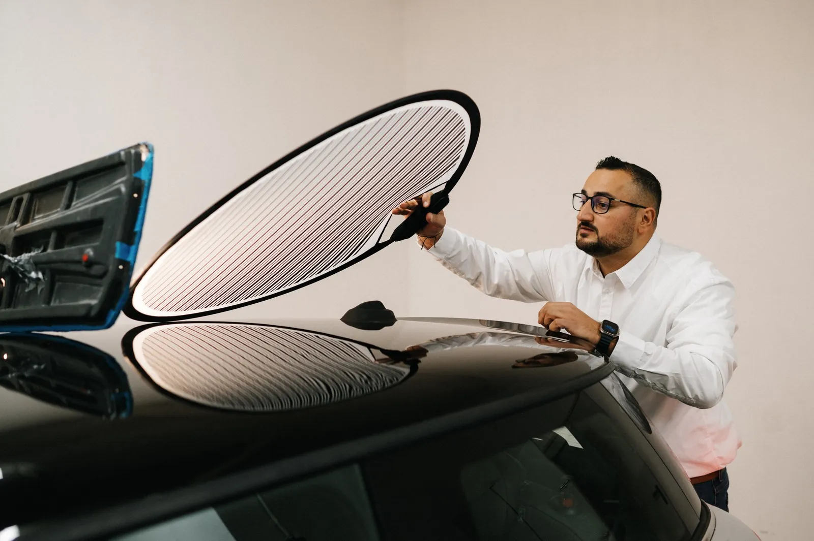 Cüneyt Kadak prüft den Lack eines schwarzen Autos mit einer Streifenlicht-Reflektortafel